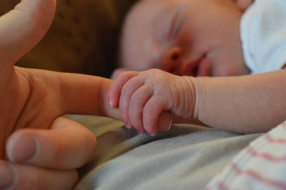  a newborn holding a woman’s finger